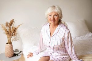 Greti entspannt lächelnd im Pyjama auf dem Bett sitzend